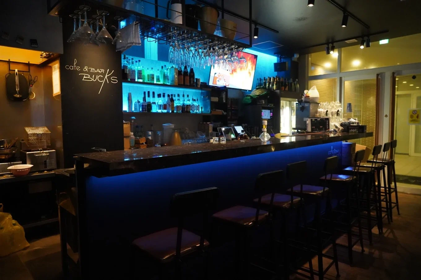 Cafe & BAR BUCKS のカウンター席。青い間接照明の下にスツールが並び、奥のバックバーに酒のボトルが並んでいる